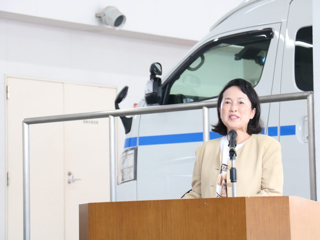救急車「HARUMIMI号」の前で、寄贈式の挨拶をする原谷治美様